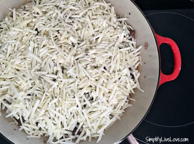 hash browns on top of ground sausage in red skillet on stovetop