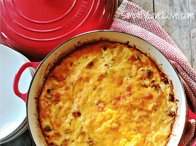 baked breakfast casserole in Le Creuset dish with red lid and kitchen towel on table